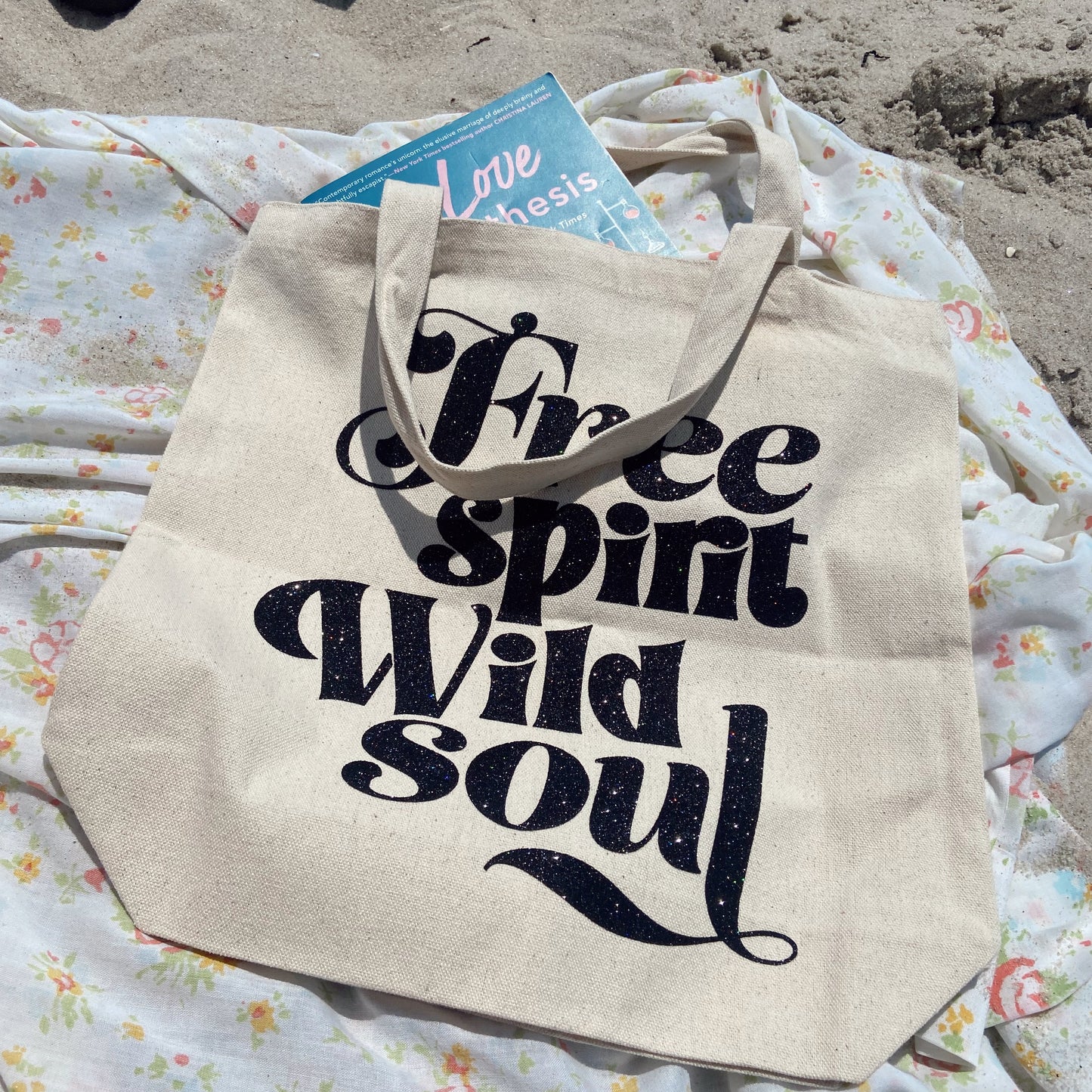 Beige tote bag with 'Free spirit, Wild soul' text on a floral blanket with sand in the background