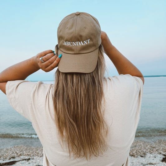 Person wearing a beige cap with 'ABUNDANT' text on a beach